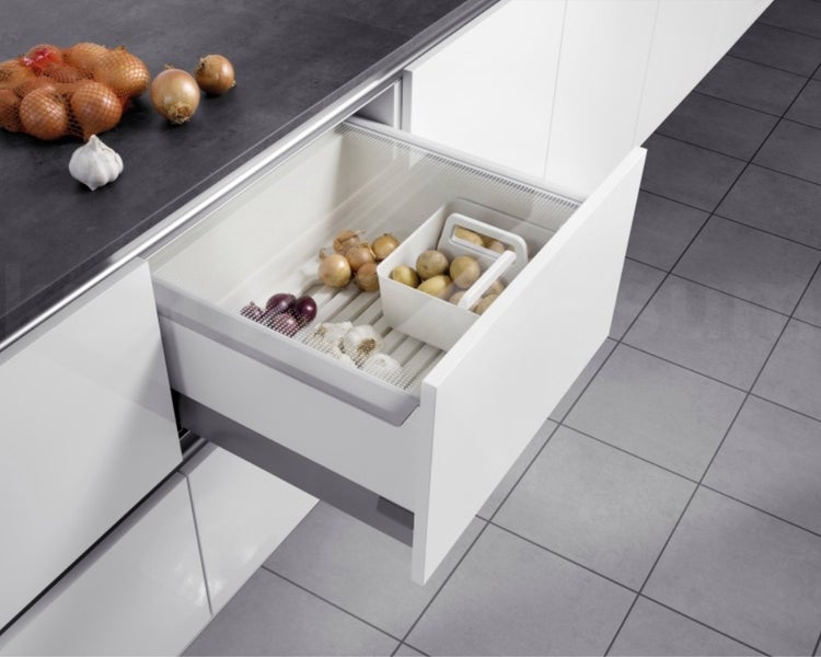 Geöffnete weiße Küchenschublade mit einem Organizer-System für Gemüse wie Zwiebeln, Kartoffeln und Knoblauch.
