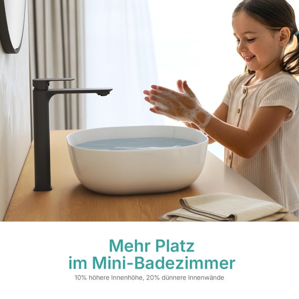 Kind wäscht Hände an einem weißen Aufsatzwaschbecken mit hoher schwarzer Armatur auf einer Holzplatte in einem hellen Badezimmer.