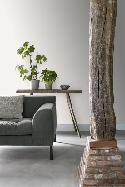 Wohnzimmer mit Sofa, Holztisch, Pflanzen und Dekoration vor einer strukturierten Tapete