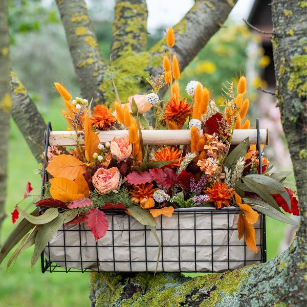 Herbstliches Blumengesteck in einem Drahtkorb auf einem Baum