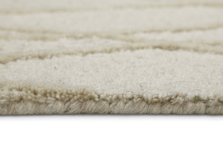Detailansicht der Kante und Struktur eines beigen Teppichs mit weichem Flor und Linienmuster.