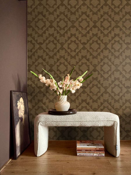 Wohnraum mit Vliestapete mit geometrischem Muster, davor eine Sitzbank aus Teddyfell mit einer Vase voller Blumen und einem eingerahmten Bild.