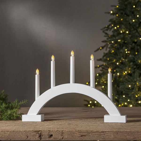 Weihnachtsleuchter mit fünf LED-Kerzen auf einem Holztisch, mit Weihnachtsbaum im Hintergrund.