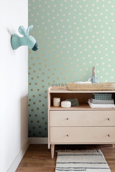 Helles Zimmer mit gepunkteter Tapete, Holzkommode mit Accessoires und einem Stofftierkopf an der Wand