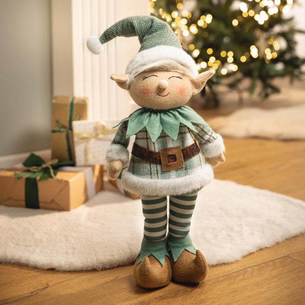 Stoffweihnachtself als stehende Dekofigur mit kariertem Outfit und Weihnachtsmütze vor Geschenken.