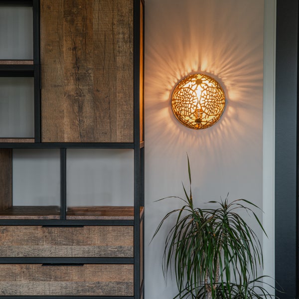 Wandleuchte aus Metall neben Holzregal und Zimmerpflanze
