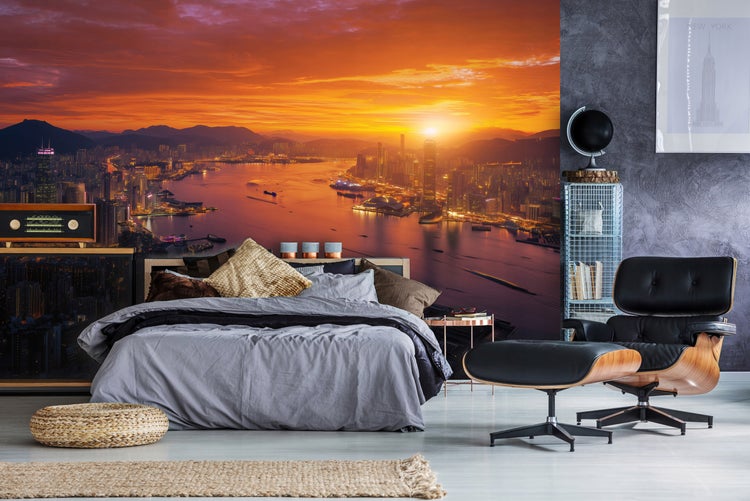 Schlafzimmer mit einem Bett vor einer Wandtapete mit einem Sonnenuntergang über einer Stadtansicht