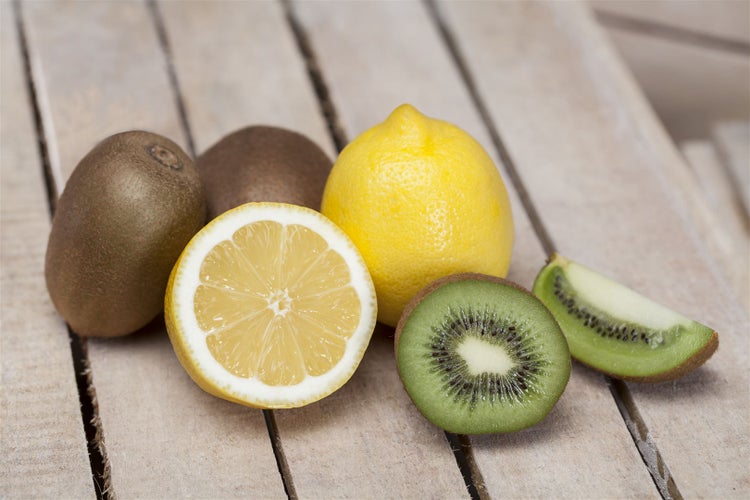 Frische Zitronen und Kiwis liegen auf einem rustikalen Holzuntergrund.