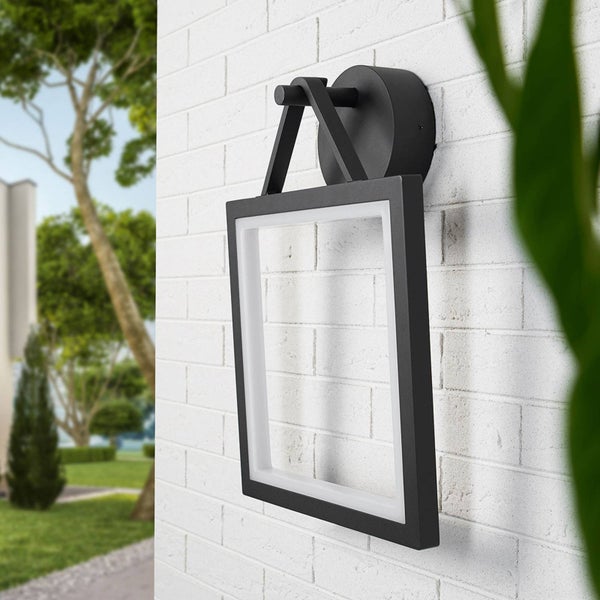 Moderne quadratische LED-Außenwandleuchte in Schwarz, montiert an einer weißen Ziegelwand in einem Garten.