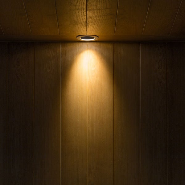 In eine Holzdecke eingelassener Einbaustrahler, der warmes Licht kegelförmig auf eine Holzwand wirft.