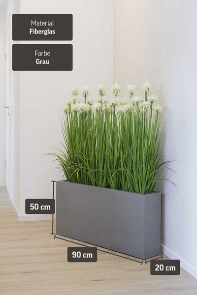 Rechteckiger grauer Pflanzkübel mit hohem Kunstgras und weißen Blumen vor einer hellen Wand.
