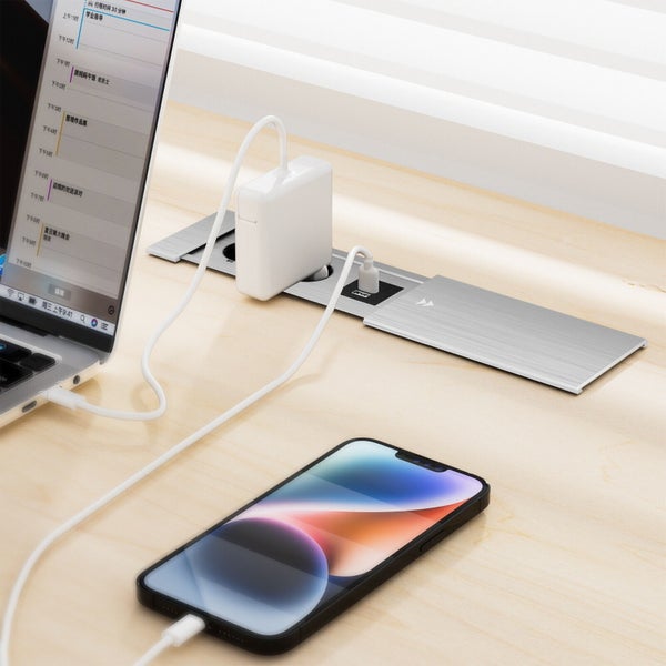 Einbau-Steckdosenleiste in Metalloptik, eingelassen in einen Schreibtisch, mit eingestecktem Netzteil und Smartphone-Ladekabel.