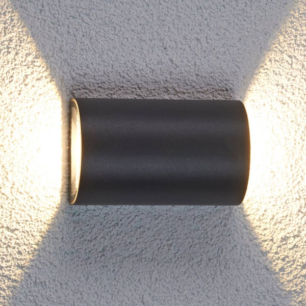 Moderne Wandleuchte in dunkler, matter Optik mit Up-and-Down-Lichteffekt an einer strukturierten Wand.