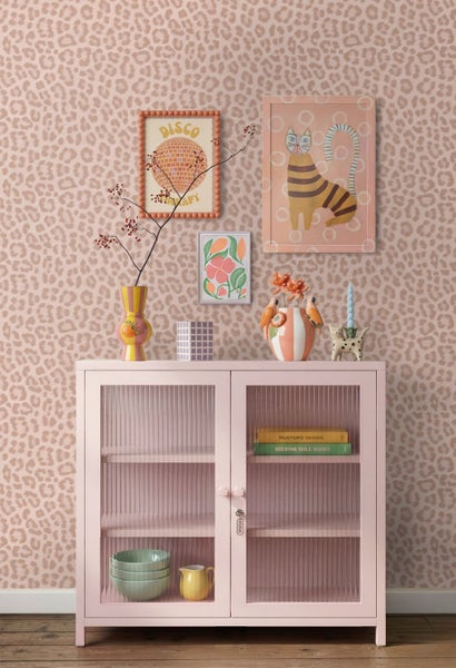 Innenraum mit Tapete in Leoparden-Optik, rosa Vitrine mit geriffeltem Glas, dekorativen Vasen und gerahmten Bildern in verspieltem Design.