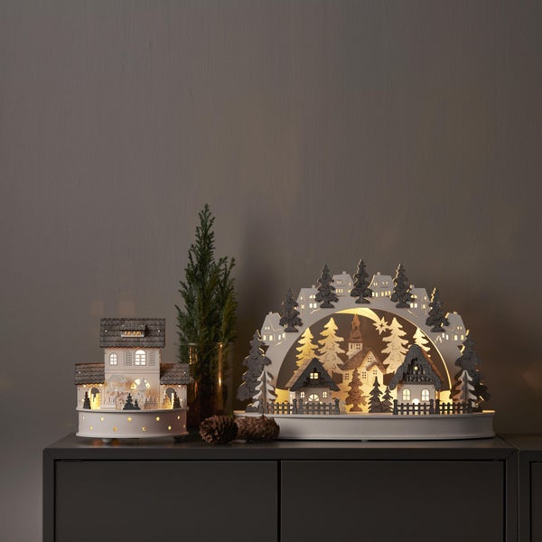 Weihnachtsdekoration mit beleuchteten Holzhäusern und Tannenbäumen auf einem Schrank