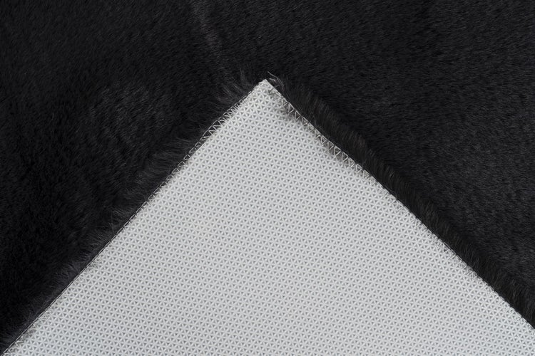 Schwarzer Kunstfellteppich, Detailansicht der weichen Textur und der rutschfesten Rückseite mit Naht.