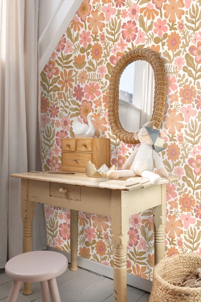Blumige Tapete im Kinderzimmer mit Holzschreibtisch, Rattanspiegel und Dekoration.