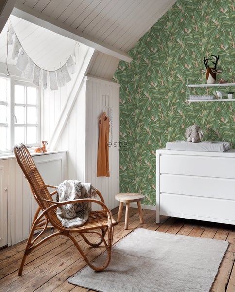 Ein helles, organisiertes Kinderzimmer mit Rattan-Sessel, Wickelkommode und botanischer Tapete.