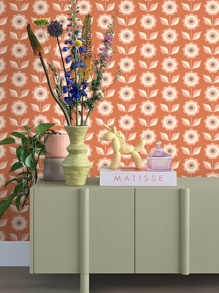 Dekorative Szene mit Blumen, Vase, Skulptur und gemusterten Tapeten auf einem Schrank