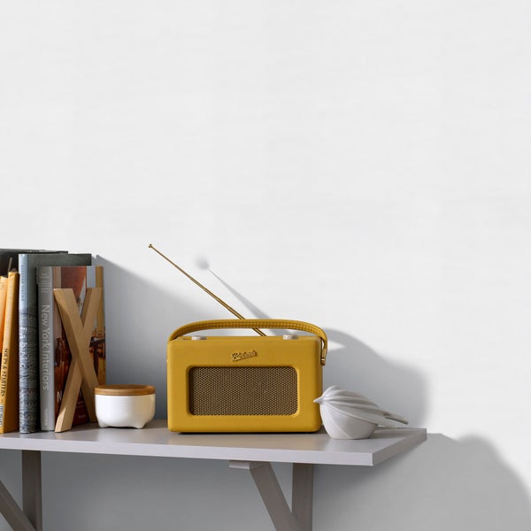 Ein ordentliches Regal mit einem gelben Retro-Radio mit Roberts Logo, Büchern mit hölzerner Buchstütze, einem Gefäß und einer Vogelfigur.