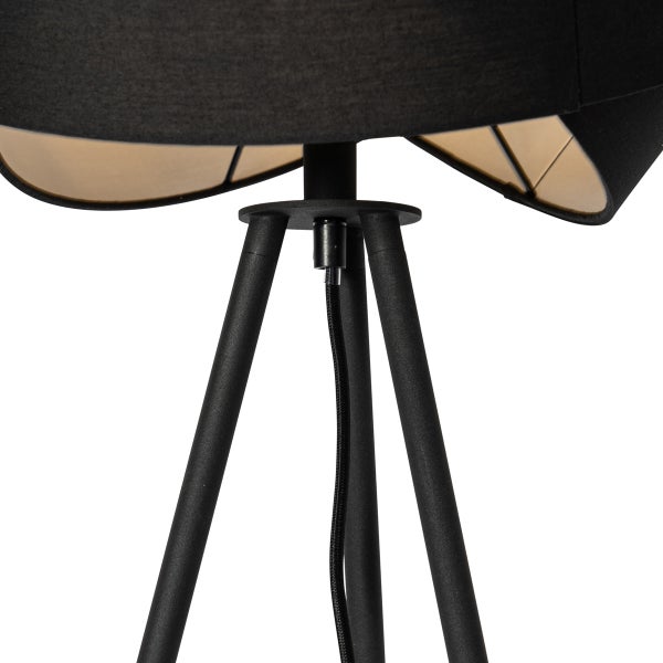 Detailansicht einer Dreibeinlampe mit schwarzem Textilschirm, goldener Innenseite und schwarzen Metallbeinen.