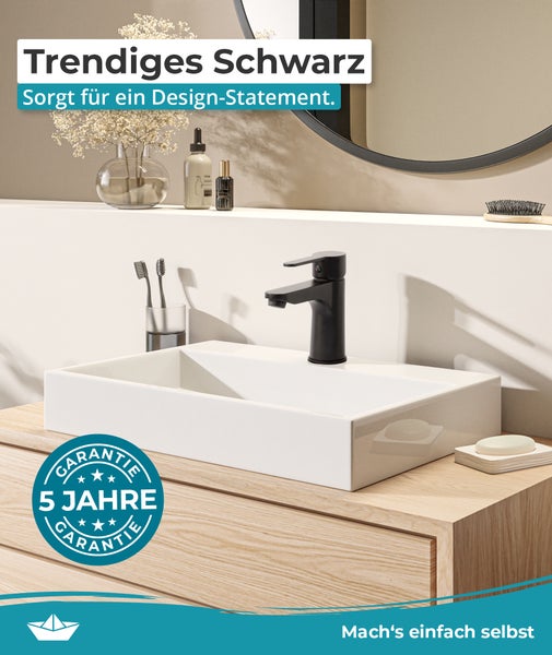 Modernes Badezimmer mit weißem Aufsatzwaschbecken, schwarzer Armatur auf Holzunterschrank, runden Spiegel und Siegel für fünf Jahre Garantie.