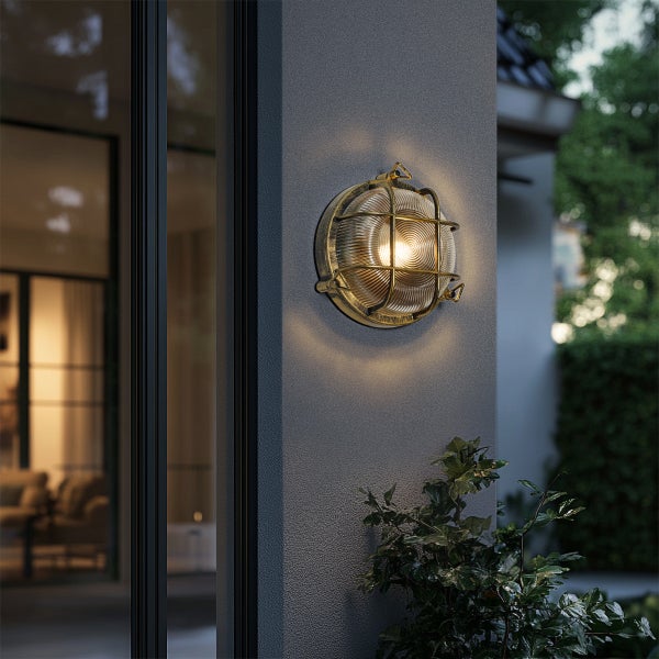 Runde Außenwandleuchte im industriellen Design mit Schutzgitter und geriffeltem Glas, montiert an einer Hauswand.