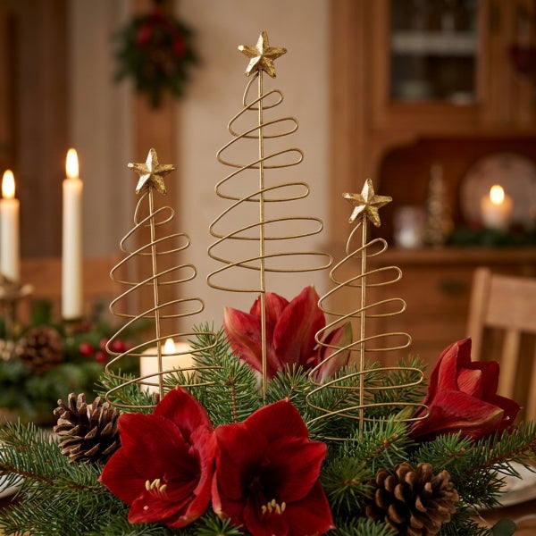 Drei spiralförmige Weihnachtsbaumfiguren aus Draht mit Sternspitze als Tischdekoration in einem festlichen Gesteck aus Tannenzweigen und Amaryllis.