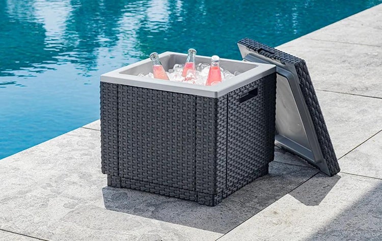 Kühlbox in Rattan-Optik mit Eis und Getränken neben einem Pool auf einer Terrasse.