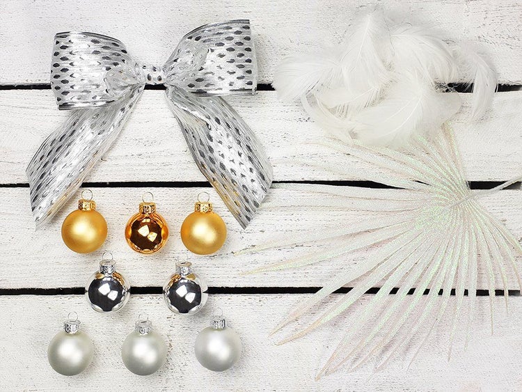 Weihnachtsbaumschmuck Set mit Schleife, Federn, künstlichem Zweig und Christbaumkugeln auf weißem Holzuntergrund.