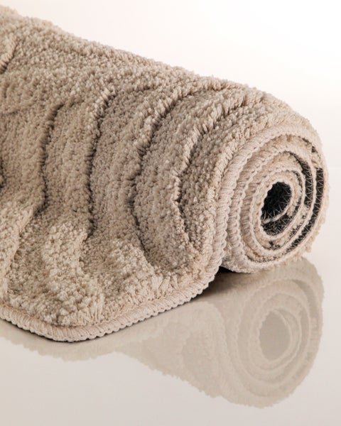 Zusammengerollte beige Badematte mit Wellenstruktur und weichem Hochflor.