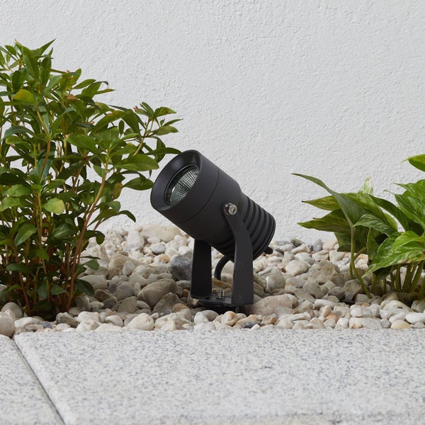 Schwarzer, verstellbarer Gartenstrahler aus Metall, positioniert zwischen Pflanzen auf hellem Kies.