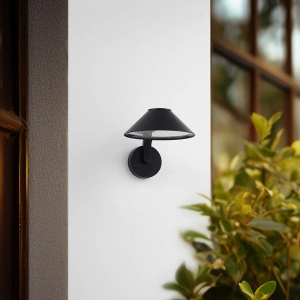Moderne schwarze Außenwandleuchte mit kegelförmigem Schirm, montiert an einer Wand neben Pflanzen.