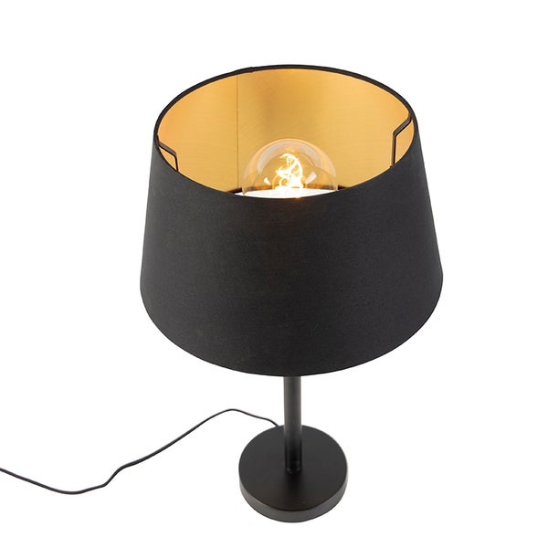 Tischleuchte mit schwarzem Textilschirm, goldener Innenseite und schwarzem Metallfuß, inklusive eingeschaltetem Leuchtmittel.