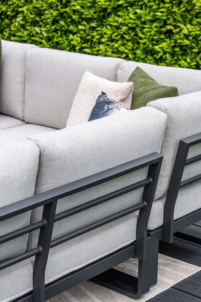 Detailaufnahme eines Gartensofas mit dunklem Metallgestell und hellgrauen Sitzkissen, dekoriert mit Zierkissen im Außenbereich.