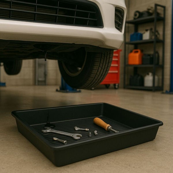 Ölauffangwanne unter einem angehobenen Fahrzeug in einer Werkstatt mit Werkzeug wie Maulschlüssel und Schraubendreher.
