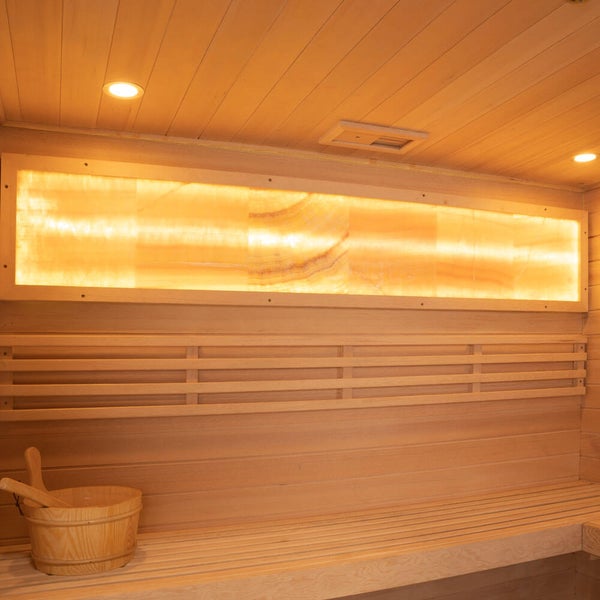Sauna Innenraum mit Holzsaunabank, Holzkübel und einer beleuchteten Salzwand zur Entspannung.