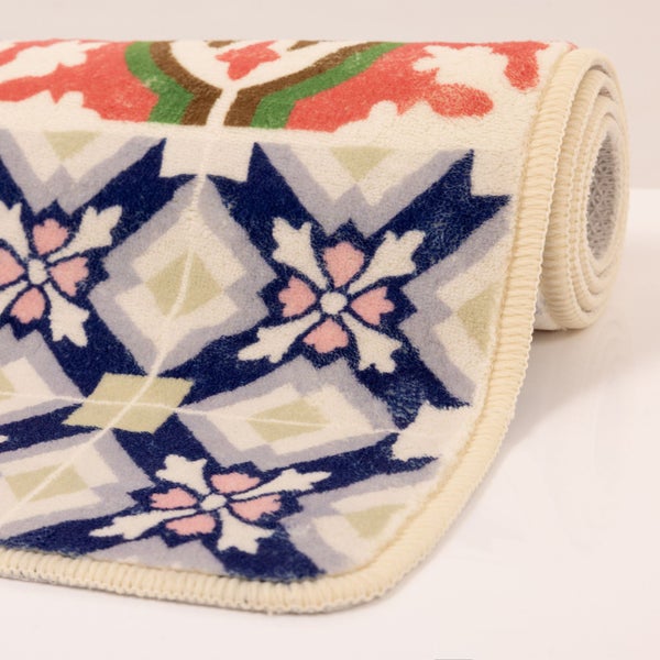 Aufgerollter Teppichläufer mit buntem Muster aus Blumen und geometrischen Formen sowie einem gekettelten Rand.