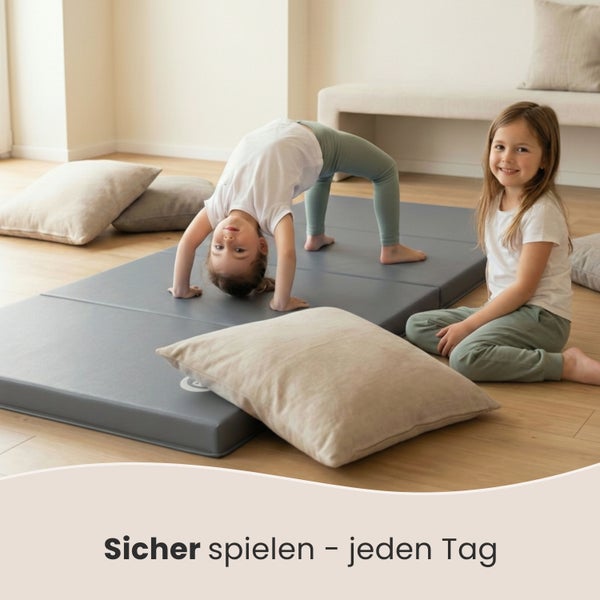 Zwei Kinder spielen auf einer grauen Spielmatte im Innenbereich.