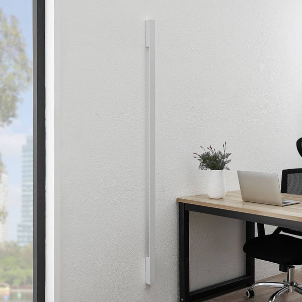 Moderne, schlanke LED-Wandleuchte vertikal montiert in einem hellen Büro neben einem Schreibtisch mit Laptop.