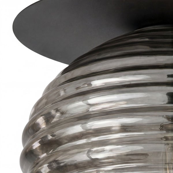 Nahaufnahme einer Leuchte mit geriffeltem Rauchglasschirm und schwarzem Metallsockel.