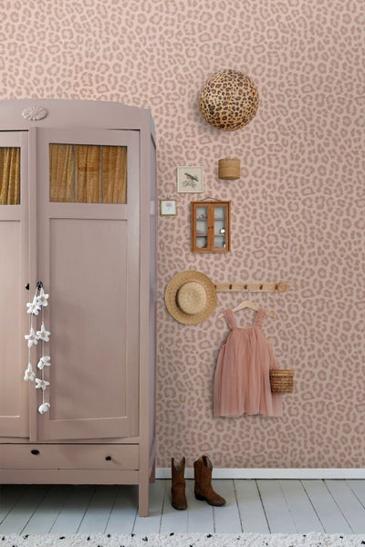 Kinderzimmer mit Leopardentapete, Vintage-Kleiderschrank aus Holz, dekorativem Hut, Kleid am Kleiderhaken und Stiefeln auf hellem Boden.