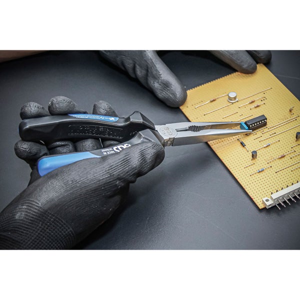 Hand mit Handschuh hält Elektronikzange über einer Platine