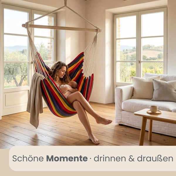 Frau mit Baby in einem bunt gestreiften Hängesessel in einem hellen Wohnzimmer mit Holzboden und großen Fenstern.
