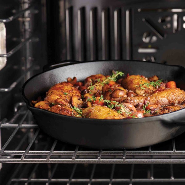 Gebratene Hähnchenschenkel mit Gemüse in einer Pfanne im Ofen.