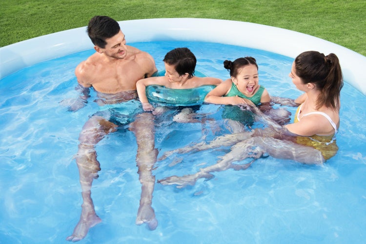 Eine Familie mit zwei Kindern entspannt in einem runden, aufblasbaren Pool mit weißem Luftring im Garten.