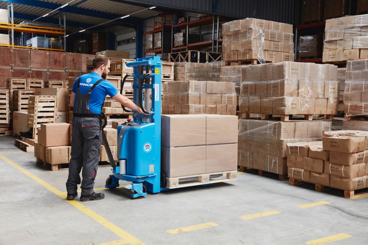 Ein Arbeiter bedient einen blauen Elektro-Hochhubwagen in einem Lagerhaus beim Transport einer Palette mit Kartons.