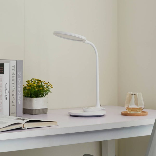Weiße LED-Schreibtischleuchte mit rundem Kopf und flexiblem Hals auf einem Schreibtisch mit Büchern und einer Pflanze.