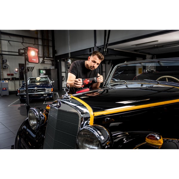 Handwerker poliert einen Oldtimer mit einer Flex Poliermaschine in einer professionellen Werkstatt unter einem LED Baustrahler.