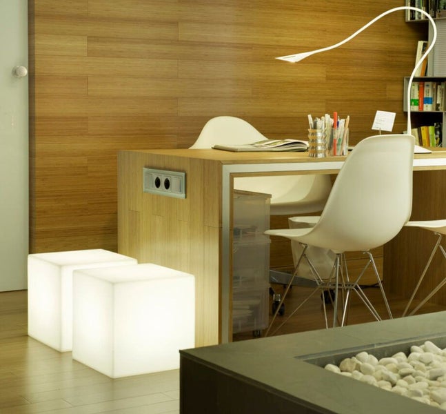 Modernes Arbeitszimmer mit Holzschreibtisch, Wandverkleidung aus Holz, zwei leuchtenden Würfeln als dekorative Elemente und Schreibtischlampe.